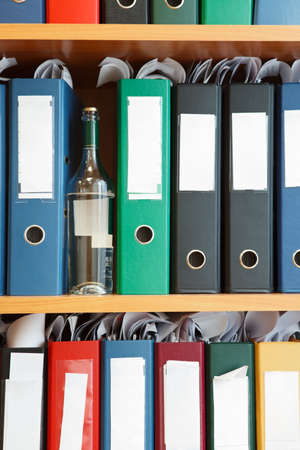 Glass bottle with alcohol hidden between file binders on shelvesの写真素材