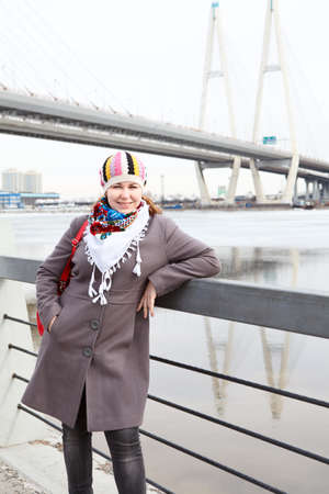 Portrait of happy young Caucasian female with red bag standing on embankment  Bridge on backgroundの写真素材