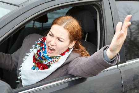 Pretty young Caucasian woman shaking hers hand and screaming sitting in carの写真素材