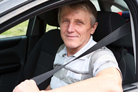 Handsome mature male fastens safety belt sitting in car on driver seat