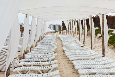 White plastic sunbeds in sandy beach under big parasolの写真素材