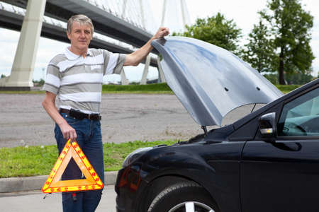 Mature man holding emergency triangle and opened car hood