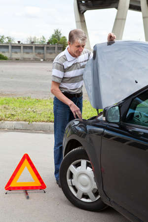 Mature man with opened car hood and emergency triangle sign on roadの写真素材