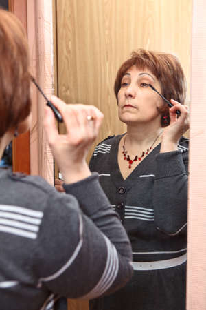 Mature Caucasian woman applying make-up against mirror in domestic roomの写真素材