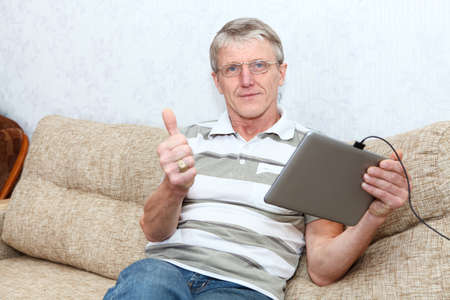 Senior Caucasian man and tablet computer  Thumb is up  Domestic room, sofa