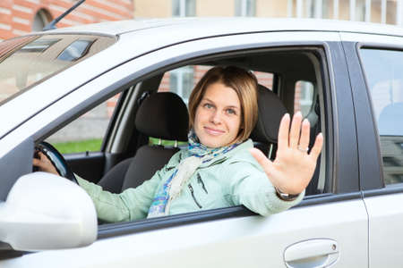 Blond hair greeting by hand and looking at camera from windowの写真素材