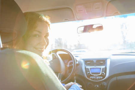 Looking back and sitting inside of car woman with sun rays in windowの写真素材