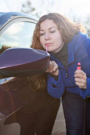 Curly hair woman applying make-up near car back side mirror against sunlightsの写真素材