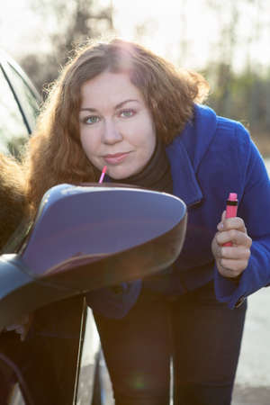 Woman applying make up near car back side mirror against sun raysの写真素材