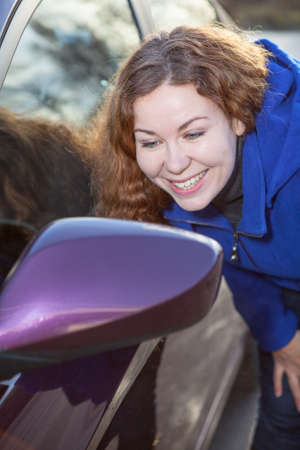 Smiling woman admire oneself in car rear-view side mirror against sunlightsの写真素材
