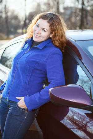 Joyful woman leaned to car smiling and looking at cameraの写真素材