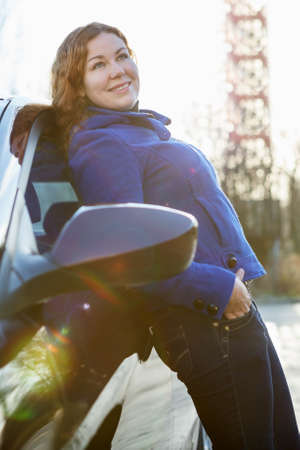Attractive girl leaned against car standing in sun lightsの写真素材