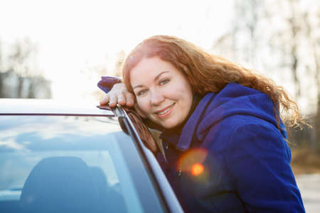 Joyful girl embracing car and looking at camera in sun lights