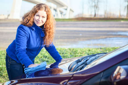 Happy smiling Caucasian woman polishing car cowlの写真素材