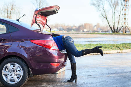Women with head crawled into opened car trunkの写真素材