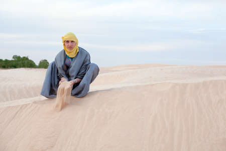Caucasian man in protection eastern clothes pouring sand by hands on desert duneの写真素材