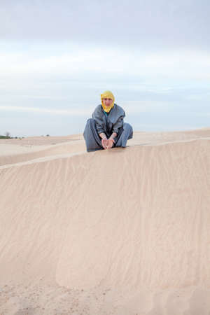 Caucasian male in protection eastern clothes pouring sand by hands on desert duneの写真素材