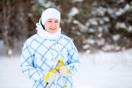 Happy young woman standing with ski poles in deep winter forestの写真素材