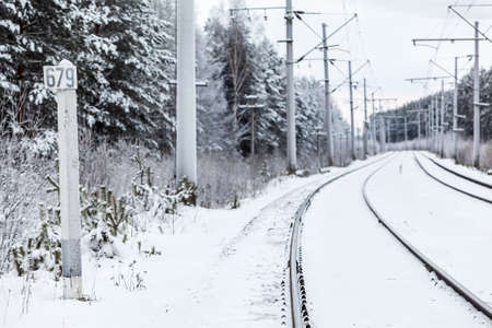 Empty electric mainline railway in winter woods with distance markの写真素材