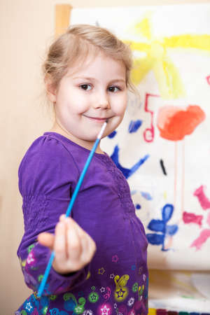 Happy preschool girl painting a picture with paints and brushの写真素材