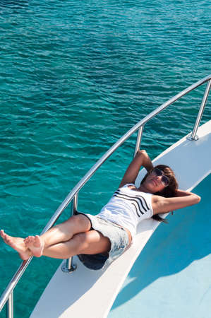 Joyous brunette woman in synglasses laying on shipboard of yachtの写真素材