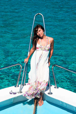 Brunette woman in dress standing on bow of yacht and looking at cameraの写真素材