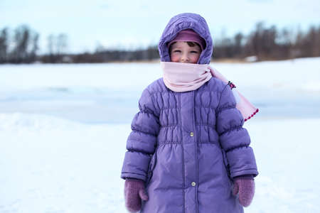 Wrapped in warm clothes small child standing outdoor in winter seasonの写真素材
