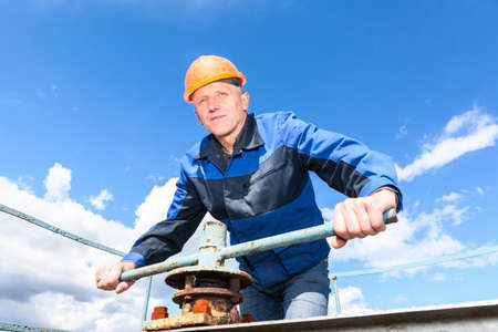 Mature Caucasian worker in a hardhat at the factory with turning the pipe valve