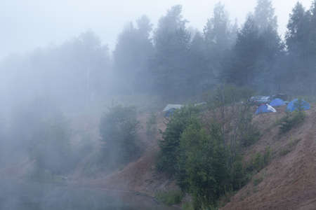 Fog on forest lake with standing tourist tents at early morningの写真素材