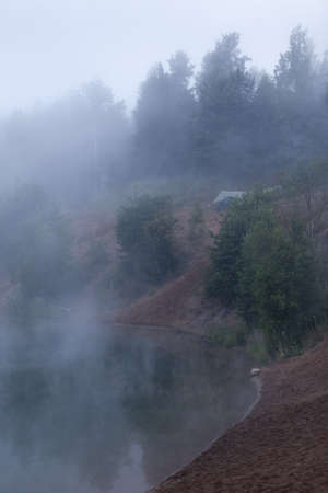 Foggy morning on forest lake with standing tourist tents on bankの写真素材