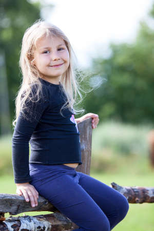 Portrait of small Caucasian girl sitting on village fence at summer dayの写真素材