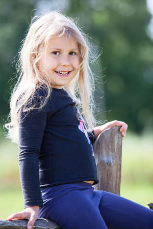 Smiling small Caucasian girl sitting on village fence at summer dayの写真素材