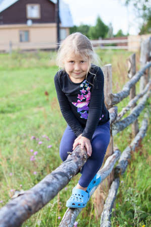 Countrygirl sitting on fence in village at summer dayの写真素材