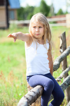 Beautiful girl pointing far away sitting on rural fenceの写真素材