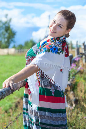 Pretty woman standing behind fence in sundress and headscarf in sunny summer dayの写真素材