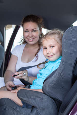 Safety children transportation with car seat in vehicle. Mother fastening daughterの写真素材
