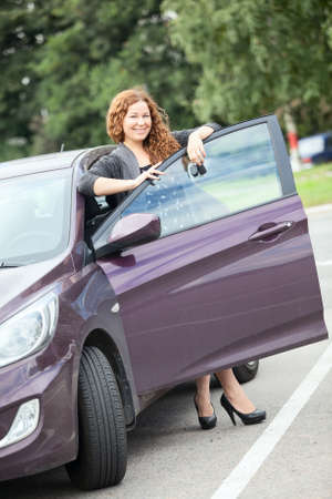 Laughing cheerful woman standing near new car with keys in handの写真素材