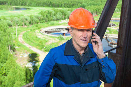 Senior man in orange hardhat calling on the phoneの写真素材