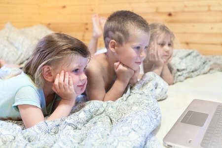 Lovely kids looking at computer monitor while laying in bedの写真素材