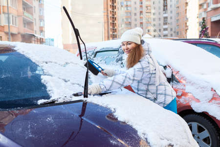 Parking area - young woman removing snow from own car with brushの写真素材