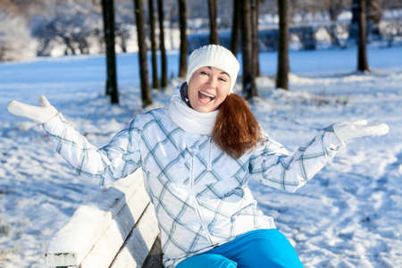 Laughing young woman on the bench with hands up, winter parkの写真素材