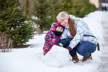 Happy mother with daughter sitting together in snow at winter parkの写真素材