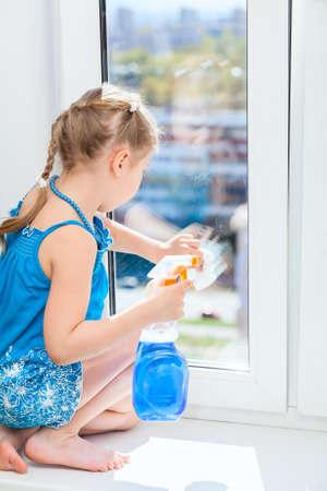 Washing windows with a rag and spray, small girl in blue dressの写真素材