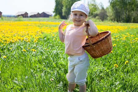 Small happy Caucasian girl standing on meadow with basketの写真素材