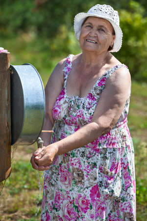 Elderly Caucasian woman washing hands in washstand outdoorの写真素材