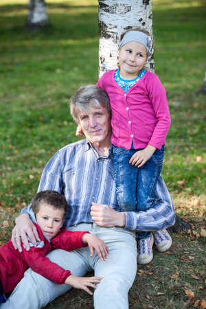 Tired grandfather with young children in autumn park on grass