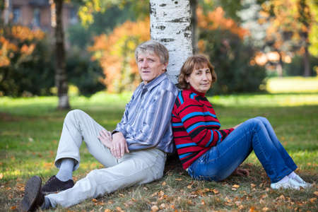 Caucasian senior couple sitting behind tree stem in autumn parkの写真素材