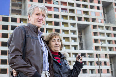 Senior couple standing with house keys in hand against apartment buildingの写真素材
