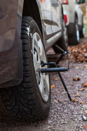Winter studded tire wheel mounting on car with jack-screw at autumnの写真素材