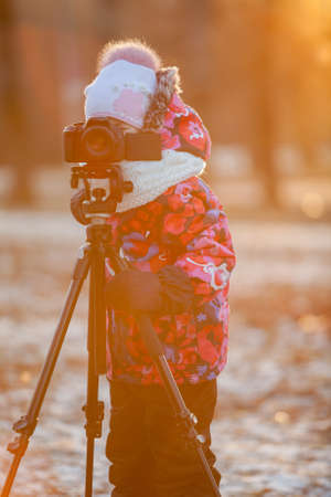Child photographer taking pictures on camera using a tripod, sunset lightの写真素材